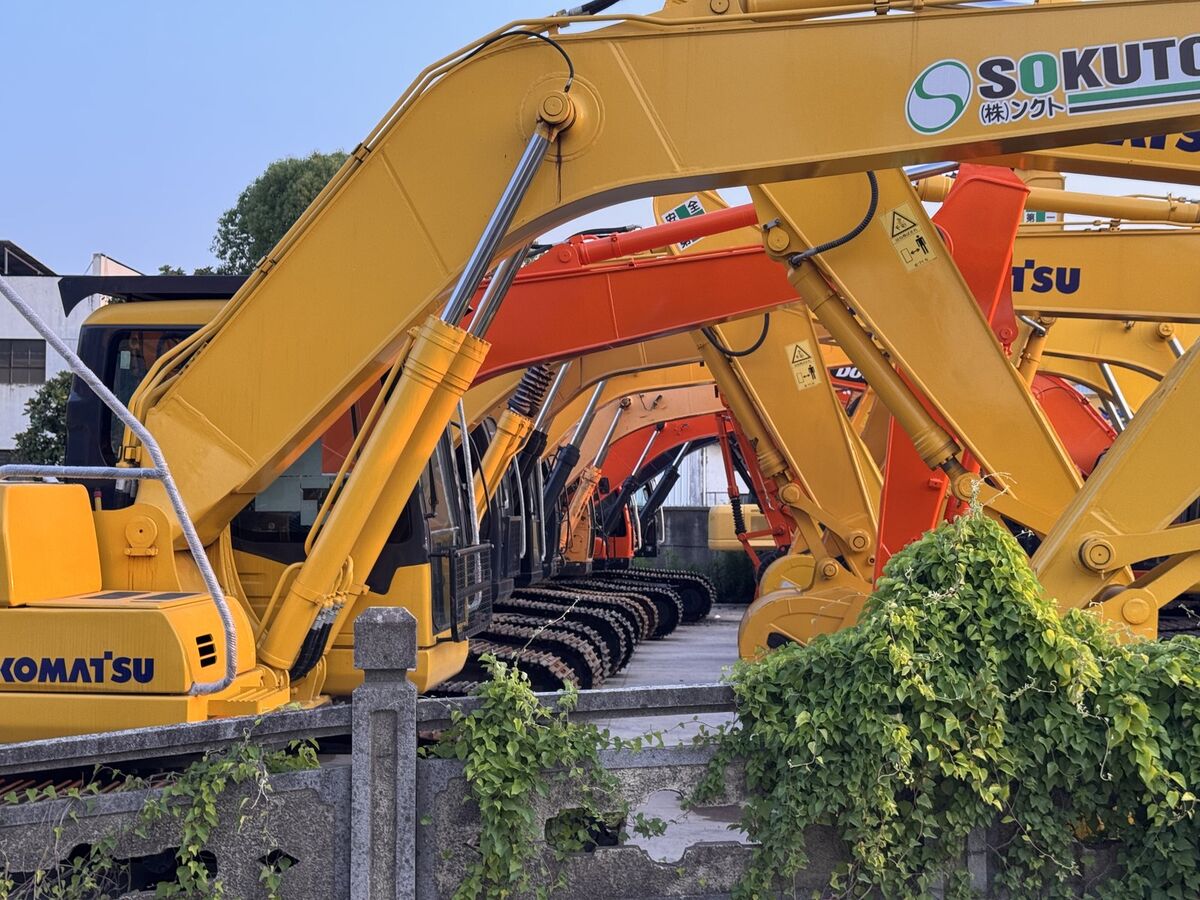 Rows of excavator booms lined up — Komatsu, Hitachi, and more
